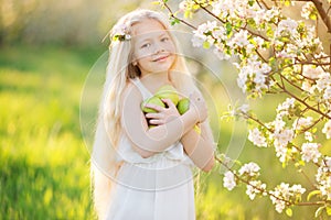 Little blonde girl in blossom garden with apples