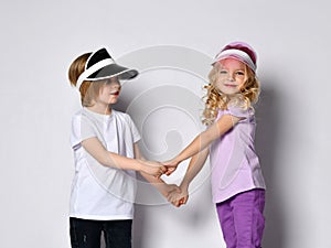 Little blonde girl and boy in colorful casual clothes and sun visors. Smiling, looking at each other, posing isolated on white