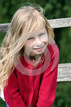 little blonde girl with curly long hair, portrait, in a red sweater in the sun