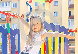 Little blonde girl with a cute smile on her face playing on the playground on a summer day