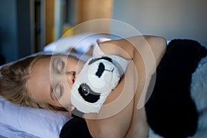 A little blonde girl in an embrace with a teddy bear panda sleeps on a large and cozy bed in a delightfully cozy hotel