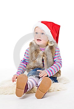 Little blonde girl in a fur jacket and a red Santa's cap sits on