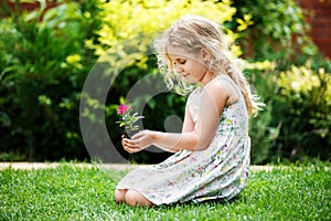 Little blonde girl holding young flower plant in hands on green background.