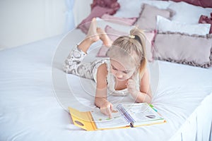 Little blonde girl lying on the bed reading a book