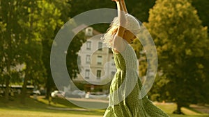 Little blonde girl performs handspring on a green park lawn on a sunny summer day