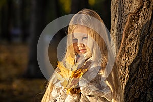 Little blonde girl in a plaid whip in the park in autumn