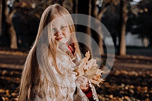 Little blonde girl in a plaid whip in the park in autumn