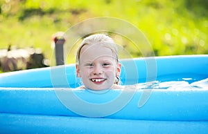 Little blonde girl in outdoor swimming pool on hot summer day.