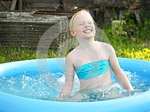 Little blonde girl playing in outdoor swimming pool on hot summer day.