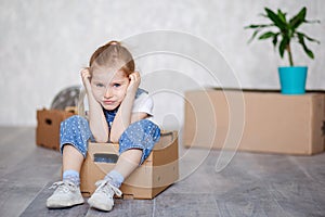 A little blonde girl plays at home in quarantine with cardboard boxes. The child moves to a new apartment, is happy and