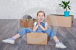 A little blonde girl plays at home in quarantine with cardboard boxes. The child moves to a new apartment, is happy and