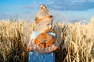 a little blonde girl in a rye field, a happy child with a rye round bread, not looking at the camera