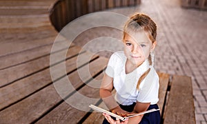 Little blonde girl in school uniform studying at the park