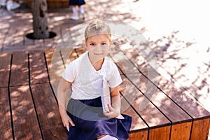 Little blonde girl in school uniform studying at the park