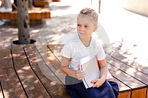 Little blonde girl in school uniform studying at the park