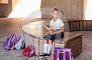 Little blonde girl in school uniform studying at the park