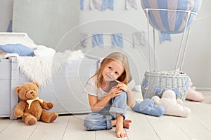 Little blonde girl is sitting on floor against background of decorative balloon. Smiling child plays in a children`s room with a t