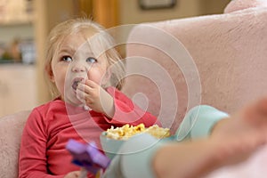 Little girl eating popcorn intently watching TV
