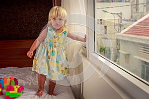 little blonde girl stands by window side-view