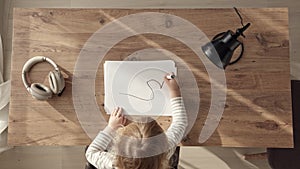 little blonde girl starts drawing with black marker, top down view of child at work desk at home or in kindergarten. Kid