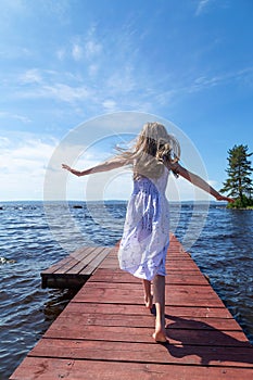 Little blonde girl in a white dress running on a wooden pier