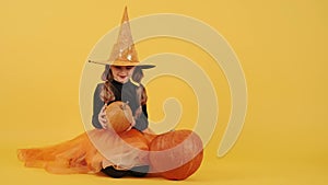 Little blonde girl in witch costume on Halloween at orange studio background