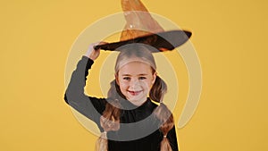 Little blonde girl in witch costume on Halloween at orange studio background