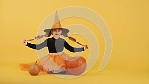 Little blonde girl in witch costume on Halloween at orange studio background