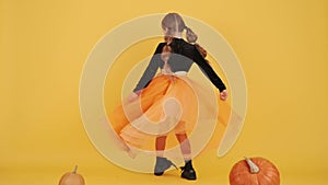 Little blonde girl in witch costume on Halloween at orange studio background