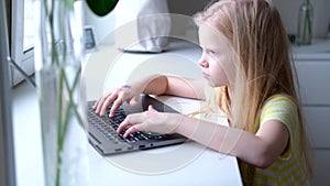 Little blonde girl working , studying or playing on laptop computer. press finger on buttons. Digital educations