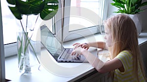 Little blonde girl working , studying or playing on laptop computer. press finger on buttons. Digital educations