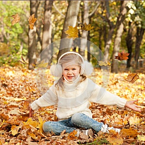 Little blonde happy girl sitting on autumn yellow maple leaves and smiling, play outdoor in autumn park