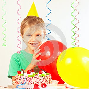 Little blonde kid in holiday cap with birthday cake and balloons