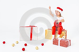 Little blonde kids in Santas hat sitting on gift boxes and holding thumb up. Isolated on white background. Holidays