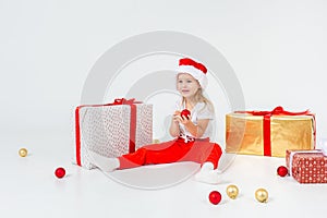 Little blonde kids in Santas hat sitting between gift boxes and playing with christmas balls. Isolated on white