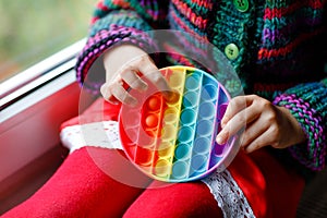 Little blonde preschool girl playing with new trend sensory toy - rainbow pop it. Antistress toy for children and adult. Colorful