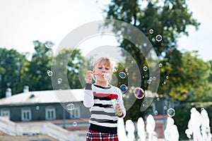 Little blondy girl playing with soap bubbles in summer park