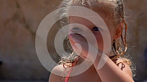 Little blue-eyed girl in a swimsuit with wet blond hair sneeze and rub her nose