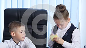 Little boss and secretary. Cheerful little boy in suit gives orders while little girl in formalwear standing near him