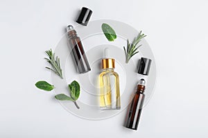 Little bottles of essential oils with different herbs on white background