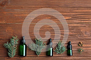 Little bottles with essential oils among pine branches on wooden background, flat lay