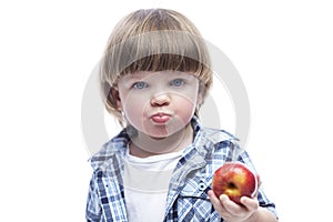 A little boy 2 years old eats an apple. Cute hungry child wearing a blue plaid shirt and a white T-shirt. Healthy foods and