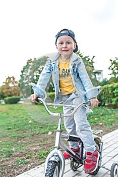 Little boy 3-5 years old, learning to ride bike, autumn day, casual warm clothes. Denim with baseball cap. Driving