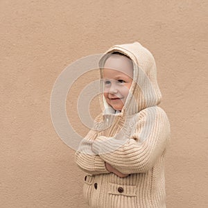 Little boy 3-5 years old, in the spring and winter in the summer, stands against the backdrop of a beige wall, in a