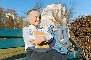 Little boy 6, 7 years old with a book. Portrait of a child with big book, reading and sitting on bench