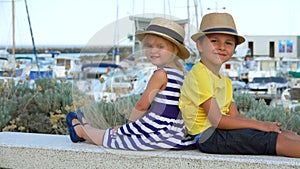 Little boy and adorable blond girl in straw hats are sitting and smiling