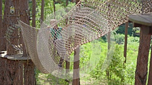 A little boy in an adventure park. He wears a safety harness. He climbs on a high rope trail. Outdoor amusement center