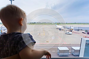 Little boy at airport looking out window at airplane.