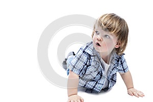 A little boy on all fours looks up in surprise. A child with a fashionable haircut wearing a blue checkered shirt and jeans.
