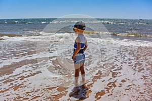 Little boy on anjuna beach with yellow sand, blue ocean and waves. North Goa, India. March 12, 2020.